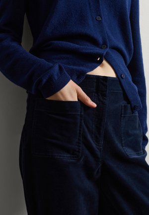 Navyblauer, weicher Cardigan mit Knöpfen, kombiniert mit navyblauen Cordhosen mit sichtbaren Taschen und Nähdetails.
