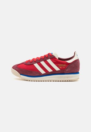 Punainen Adidas SL 72 -lenkkari valkoisilla raidoilla, punaisilla nauhoilla, mokkanahkauksilla ja sinikermanvärisellä pohjalla, esitetty vasemman sivuprofiilinäkymässä.