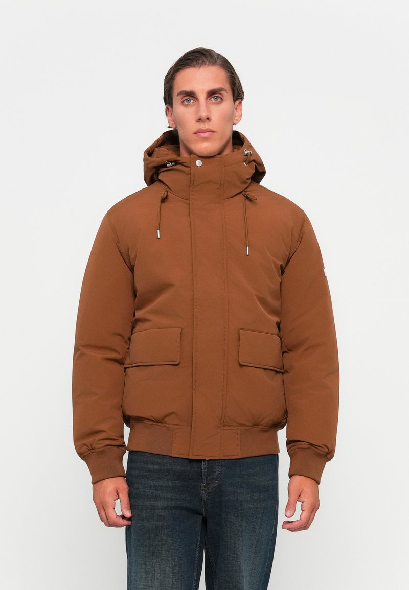 Brązowa pikowana kurtka z kapturem, z dwiema przednimi kieszeniami, sznurkiem do regulacji i ściągaczem na dole. Gładka tekstura i jednolity kolor.