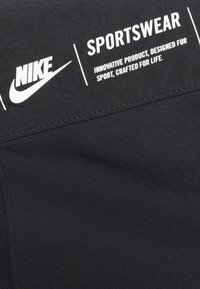 Svart Nike sportkläder tyg med texturerad yta. Har en framträdande vit logotyp och text som säger "SPORTKLÄDER" och "INOVATIV PRODUKT."