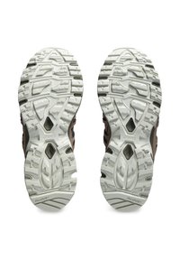 Trailrunning schoenen hebben een bruin en zwart bovenwerk met een gestructureerde witte buitenzool, en tonen multidirectionele noppen voor verbeterde grip.