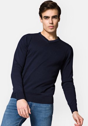Granatowy sweter v-neck z prążkowanej dzianiny, z długimi rękawami i dopasowanym krojem. Subtelny detal logo na klatce piersiowej.