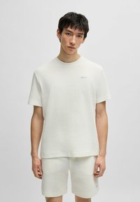 Witte textuur kortebloem T-shirt met een subtiel ruitpatroon en ronde halslijn, met een klein geborduurd logo op de linkerkant van de borst.