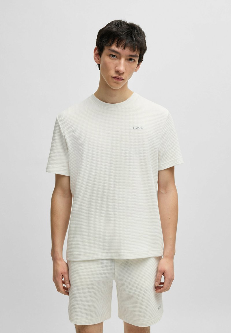 T-shirt bianco a maniche corte con una sottile trama a griglia e scollatura rotonda, caratterizzato da un piccolo logo ricamato nella parte sinistra del petto.