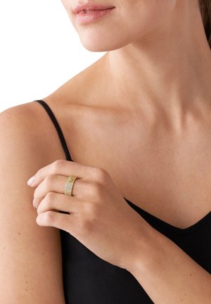 Gold ring featuring a textured band with sparkling accents, worn on a hand with a neutral nail color, against a light background.