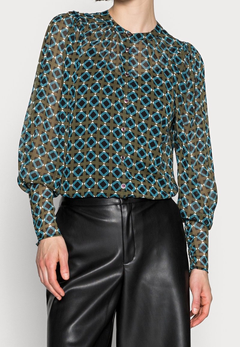 Transparent knapp-up blus i khaki med ett geometriskt blått mönster, ballongärmar och rund halsringning, kombinerad med svarta läderbyxor.