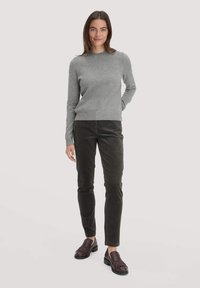 Grauer Strickpullover mit Rundhalsausschnitt, kombiniert mit dunkelgrünen Cordhosen und dunkelbraunen Slippern mit Fransenakzenten.