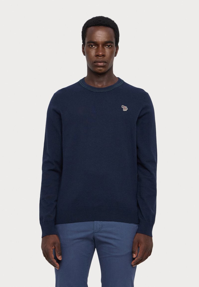 Navy blue crewneck sweater with long sleeves, made of knitted fabric. Features a small embroidered design on the chest and ribbed cuffs.