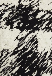 Svart och vit stickad tyg med ett strukturerat mönster som påminner om penseldrag. Mjuk textur med en kontrasterande färgschema.