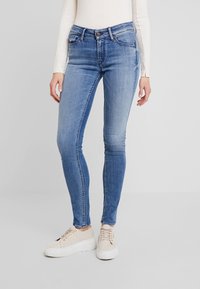 Blå skinny jeans i denim med hög midja, femfickorsdesign och smal passform, kombinerat med ljusa sneakers.