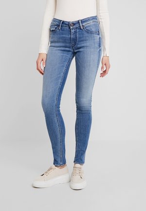 Vaqueros ajustados azules de denim, con una cintura alta, diseño de cinco bolsillos y corte slim, combinados con zapatillas de color claro.