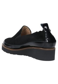 Scarpa nera slip-on con tomaia in suede, dettagli lucidi in vernice e una spessa suola in gomma. Presenta un interno morbido e una linguetta sul tallone.