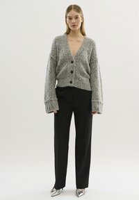 Grå texturerad cardigan med djup V-ringning och fyra knappar, ihop med svarta byxor och silverfärgade pumps med spetsig tå. Vid ärmar och avslappnad passform.