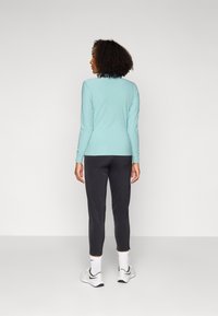 Jasnoniebieska bluzka z długim rękawem i okrągłym dekoltem, zestawiona z czarnymi zwężanymi spodniami. Modelka ma na sobie białe buty z czarnymi akcentami oraz widoczne białe skarpetki.