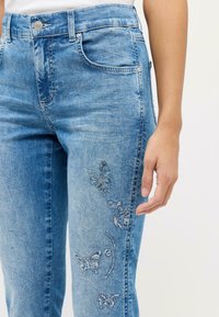 Helle blaue Jeans aus Denim mit Schmetterlingsstickerei an der Seite, im Fünf-Taschen-Stil und einer figurbetonten Silhouette.