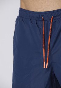 Pantaloni da bagno blu navy con cintura elastica, dotati di lacci arancioni e tessuto liscio e leggero.