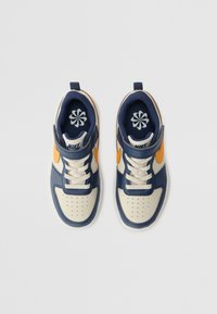 Nike-tennarit siniset ja kermaiset, joissa on rei'itetty varvasosa, oranssit korostukset, valkoiset nauhat ja vahvistettu kantapää. Kukallinen logo sisäpohjassa.
