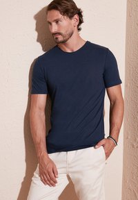 Tricou bleumarin cu guler rotund, confecționat dintr-un material ușor, având mâneci scurte și un design ajustat, asortat cu pantaloni de culoare deschisă.