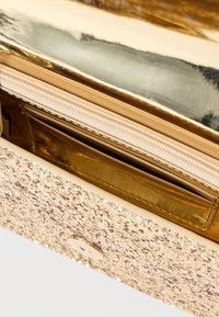 Χρυσό τσαντάκι clutch με υφή και λαμπερή, μεταλλική εσωτερική επένδυση. Περιλαμβάνει φερμουάρ σε θήκη και θέσεις για κάρτες.