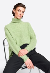 Hellgrüner, gerippter Rollkragenpullover mit langen Ärmeln, kombiniert mit schwarzen Hosen. Weiche Textur, lockerer Schnitt und leicht übergroßes Design.