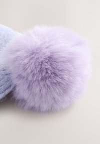 Miękki, puszysty, jasnofioletowy pompon przymocowany do jasnoniebieskiej dzianiny, na neutralnym tle.