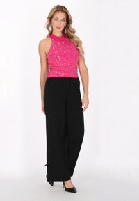 Top halter rosa aderente con un design texturizzato e accenti metallici, abbinato a pantaloni neri a vita alta con gamba larga e tacchi neri.