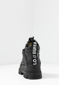 Zapatilla negra de caña alta con parte superior de cuero texturizado, cuello acolchado, suela gruesa y una pestaña de logo prominente en la parte trasera.