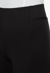 Schwarze Leggings aus dehnbarem Stoff, mit hohem Bund und einer dezenten Seitentasche. Glatte Textur mit nahtlosem Design.