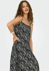 Rochie neagră cu un model de puncte albe, având bretele subțiri, croială relaxată și o siluetă fluidă. Textură de stofă moale.