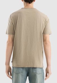 Beige bavlněné tričko s krátkými rukávy, kulatým výstřihem a minimálním prošíváním na okrajích. Měkká textura a volný střih.