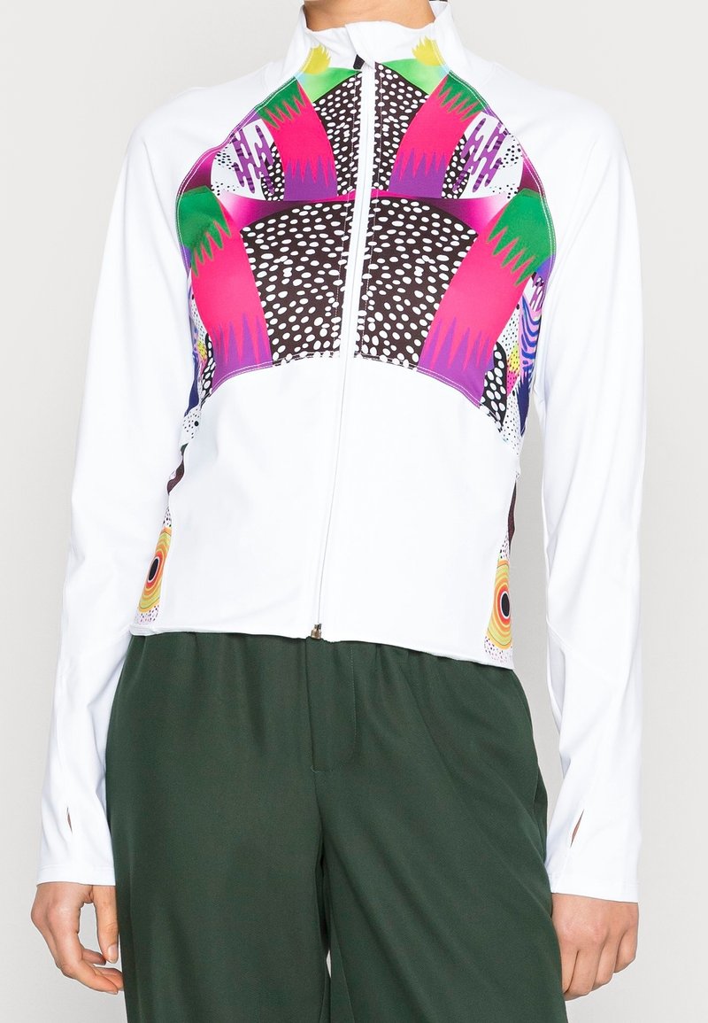 Witte ritsjack met kleurrijke geometrische patronen in roze, groen en zwart. Lange mouwen met duimgaten, gladde textuur.