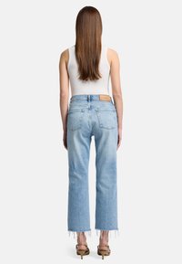 Jean en denim bleu clair, taille haute, avec une coupe droite, ourlets bruts et deux poches arrière, porté avec un haut débardeur blanc et des talons.