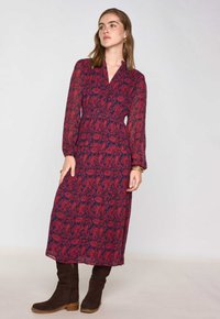 Abito lungo bordeaux con motivo floreale, caratterizzato da maniche lunghe, scollo a V e vita vita, abbinato a stivali in suede marroni al ginocchio.