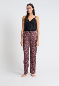 Czarna satynowa kamizelka z koronkowym wykończeniem, zestawiona z spodniami w kwiatowy wzór w odcieniach różu i czerni. Spodnie mają luźny krój i elastyczny pas ze sznurkiem.