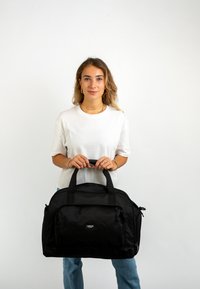 Černý sportovní vak s hladkým povrchem, dvěma vrchními ušima, přední kapsou na zip a značkovou nálepkou. Jednoduchý, funkční design vhodný na cestování.