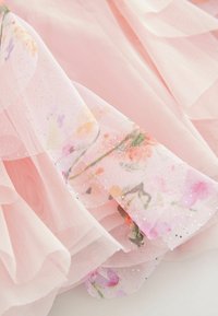 Rosa Netzstoff, der mit floralen Mustern in sanften Farbtönen und subtilen Glitzerakzenten geschichtet ist, mit einer luftigen, leichten Textur und schimmernden Kanten.