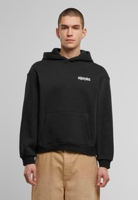 Schwarze Kapuzenjacke aus Baumwollmischung mit Kängurutasche und gerippten Bündchen. Mit weißem Logotext auf der Brust.