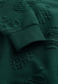 Zielona bluza z teksturowanym wzorem ananasów, prążkowanymi mankietami i miękką powierzchnią materiału.