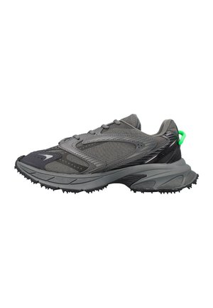 Zapatilla deportiva gris con suela texturizada, parte superior de malla y material sintético, y una pequeña lengüeta de tirador en color verde brillante en el talón.