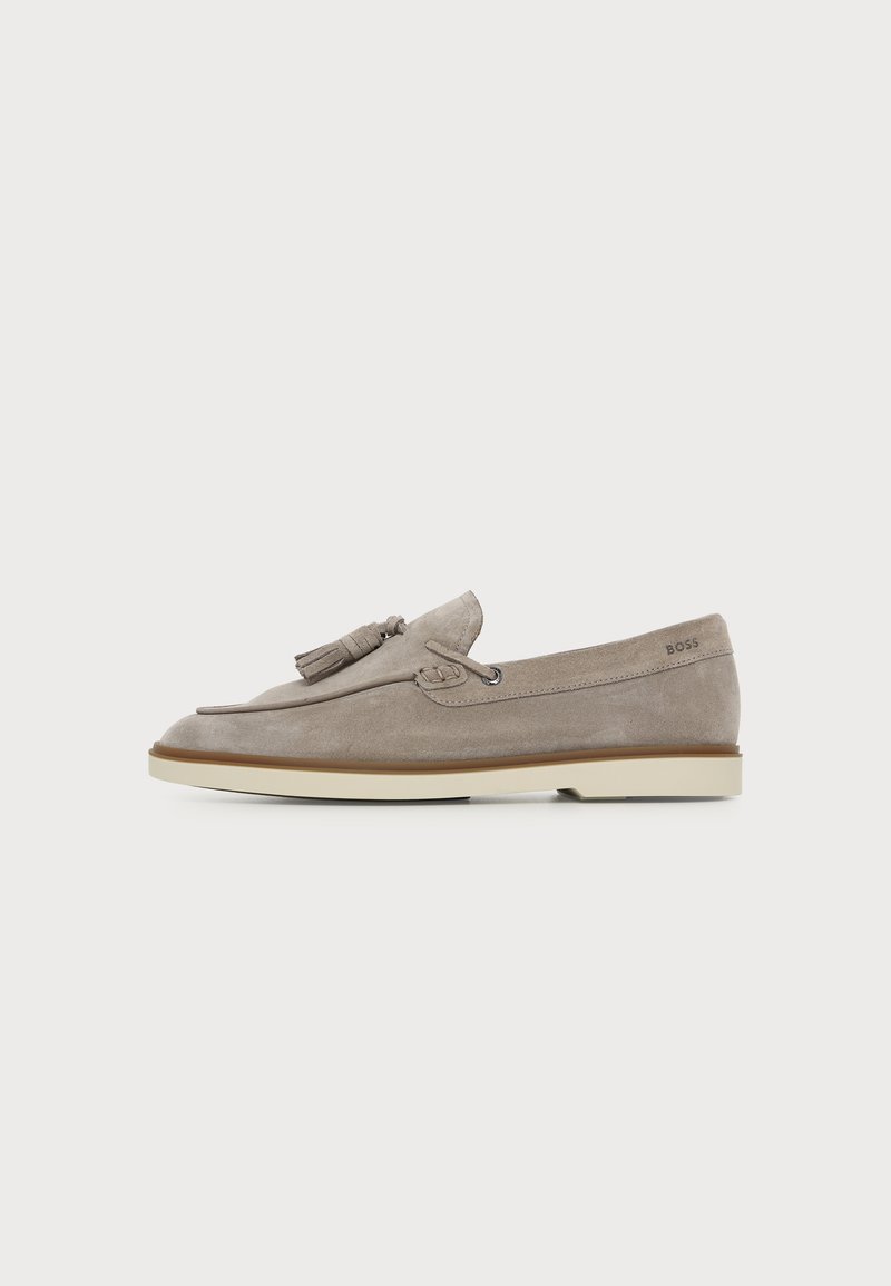 Mocassin homme en daim marron clair avec détail pompon et semelle en caoutchouc crème, vue de côté sur fond uni.