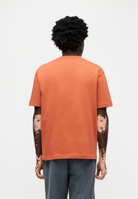 Μπλουζάκι με κοντά μανίκια σε άνετη εφαρμογή, από βαμβάκι σε καμένο πορτοκαλί χρώμα. Κλασικός στρογγυλός λαιμός και ίσια γραμμή στο τελείωμα, με απαλή υφή.