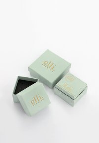 Green cardboard gift boxes with gold lettering, including a square box with a black interior and various sizes stacked together.