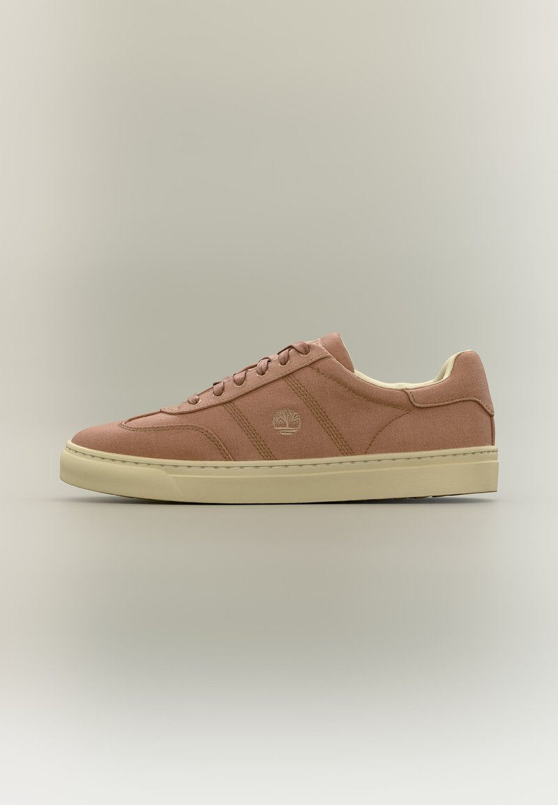 Žemo profilio zomšiniai sportbačiai blankiai rožinės spalvos su smėlio spalvos padu, raišteliais ir siuvinėtu prekės ženklo logotipu šoninėje dalyje.