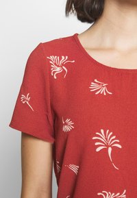 Top rosso a maniche corte realizzato in tessuto testurizzato, con motivi floreali bianchi su tutta la superficie e scollatura tonda.