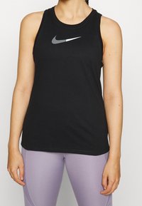 Camiseta atlética sin mangas negra con un escote redondo y un logotipo gris de Nike en el pecho. El material parece suave y ajustado.
