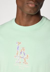 Mint green t-shirt featuring a multi-colored floral and paisley embroidered "LA" logo and text "Los Angeles Dodgers." Soft cotton fabric.
