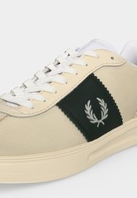Μπεζ και λευκό sneaker χαμηλού πατούμενου με λευκά κορδόνια και σκούρο πράσινο πλαϊνό πάνελ με λευκό λογότυπο δάφνινο στεφάνι.