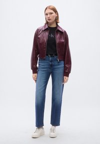 Μπουφάν από δέρμα μπορντό, μαύρο T-shirt, ψηλόμεσο τζιν μπλε χρώματος και λευκά αθλητικά παπούτσια. Ομαλή υφή με κλείσιμο με φερμουάρ και φαρδύ γιακά.