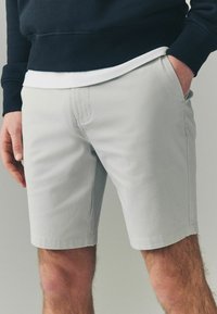 Pantalones cortos de hombre en gris claro, confeccionados en una tela suave, con bolsillos laterales, un corte recto y un acabado limpio en el dobladillo.