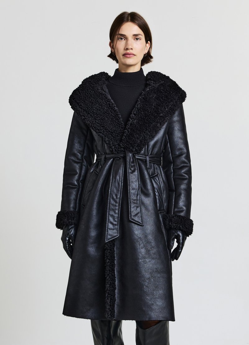 Cappotto in pelle nera con un colletto in pelliccia sintetica nera texturizzata, vita con cintura e dettagli in pelliccia sintetica abbinati sui polsini.